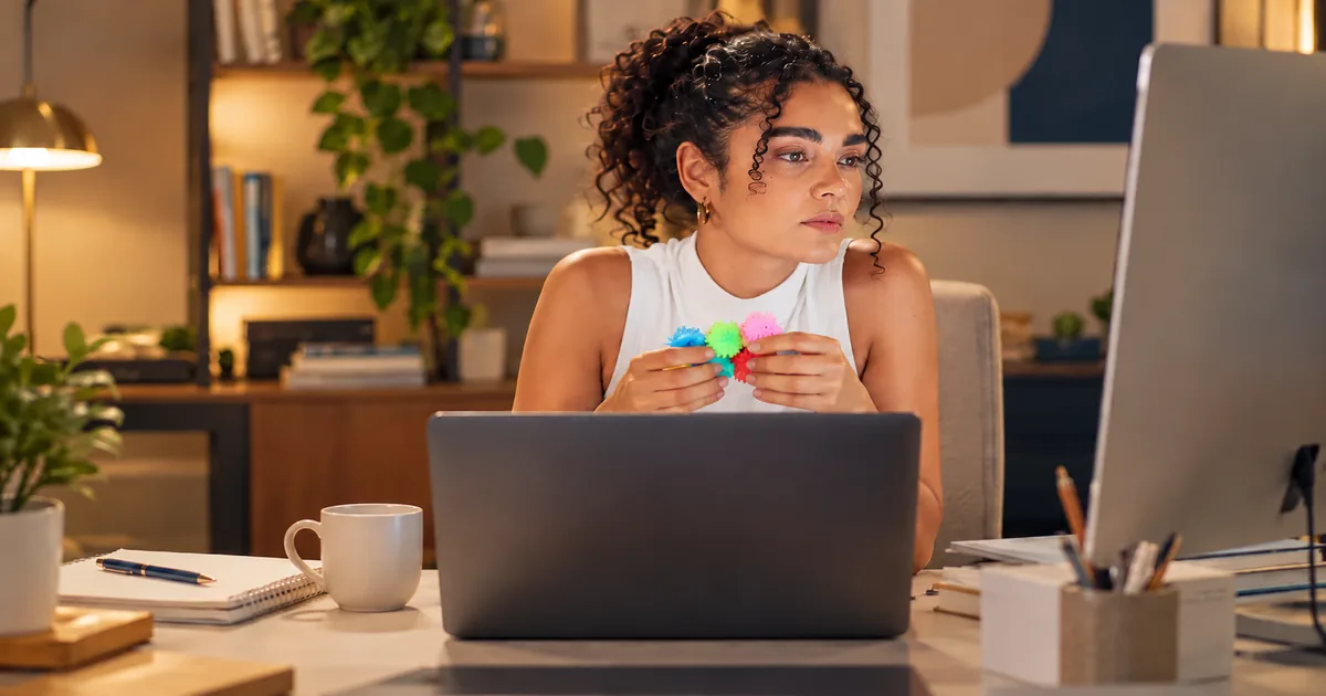 Mulher adulta em ambiente de trabalho segurando objeto colorido durante momento de concentração.